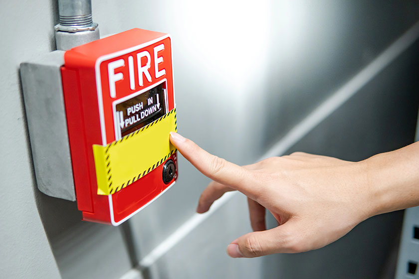 Hand pointing at fire alarm switch on the wall